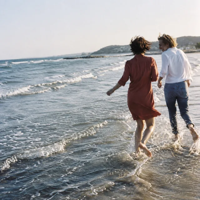 Two friends splashing in the surf, one in a red shirt dress