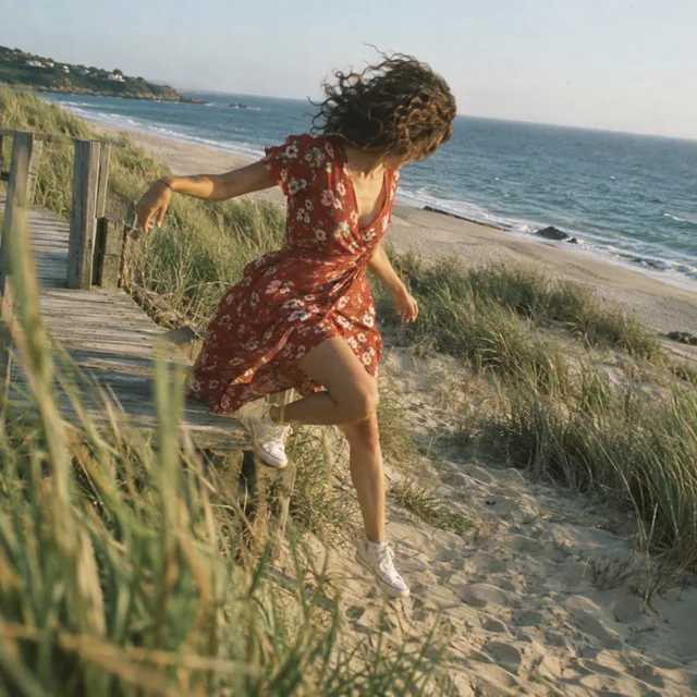 Woman in a red floral dress jumping from a dune boardwalk