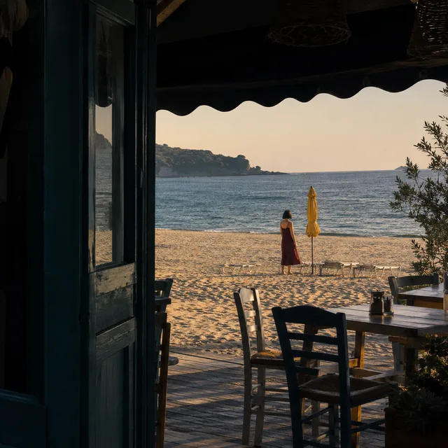 Small figure in a wine-red dress framed by a beach cafe doorway